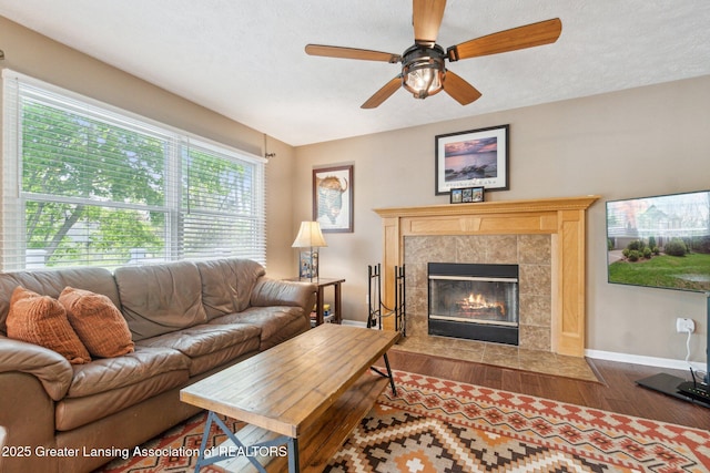 living area with dark wood-type flooring, baseboards, a fireplace, ceiling fan, and a textured ceiling