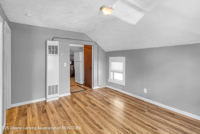 922 Dakin St, Lansing, MI 48912 - unfurnished bedroom featuring freestanding refrigerator, lofted ceiling, baseboards, wood finished floors, and a textured ceiling