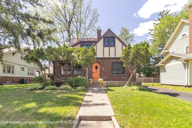 514 W St, Lansing, MI 48915 - tudor-style house featuring brick siding, a front yard, a chimney, and cooling unit
