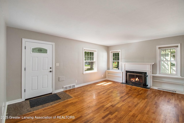 2119 Grant St, Lansing, MI 48910 - unfurnished living room featuring wood finished floors, plenty of natural light, a fireplace with flush hearth, and baseboards