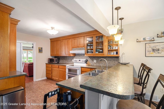 12197 W Greenfield Rd, Lansing, MI 48917 - kitchen featuring double oven range, a sink, a peninsula, a breakfast bar area, and backsplash