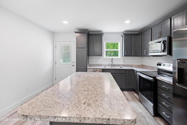 2107 Reo Rd, Lansing, MI 48910 - kitchen with appliances with stainless steel finishes, a sink, a center island, light countertops, and light wood finished floors