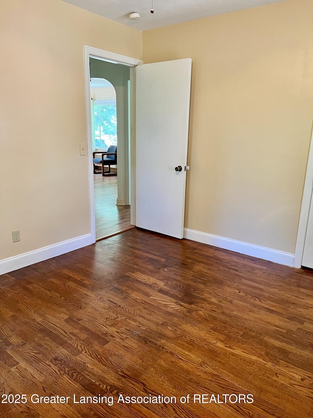 341 W Saginaw St, East Lansing, MI 48823 - empty room with dark wood-type flooring, arched walkways, a smoke detector, and baseboards
