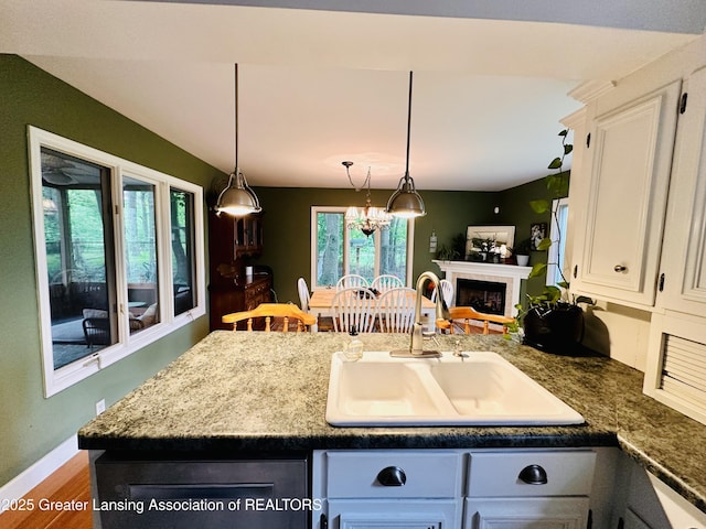 812 Dryer Farm Rd, Lansing, MI 48917 - kitchen featuring a sink, a peninsula, white cabinetry, decorative light fixtures, and wood finished floors