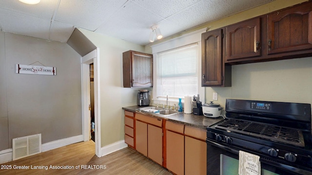 1023 Bement St, Lansing, MI 48912 - kitchen featuring black range with gas stovetop, a sink, dark countertops, light wood-style flooring, and baseboards