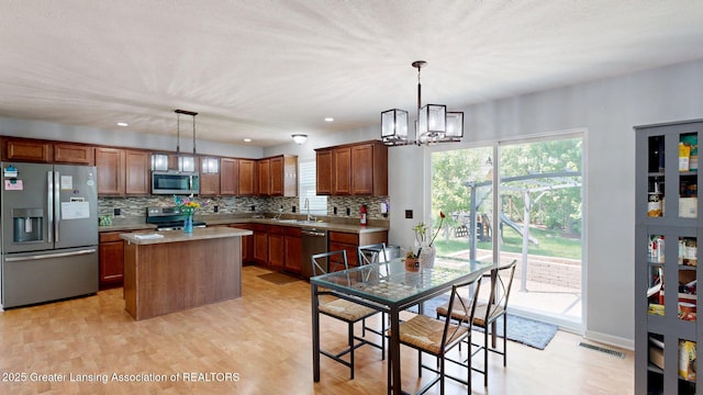 1055 Oakwood Dr, Dewitt, MI 48820 - kitchen with stainless steel appliances, a chandelier, decorative backsplash, a kitchen island, and light wood-style flooring