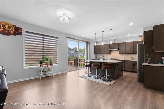 5651 Copper Creek Dr, Haslett, MI 48840 - kitchen with light countertops, dark brown cabinets, freestanding refrigerator, under cabinet range hood, and a breakfast bar