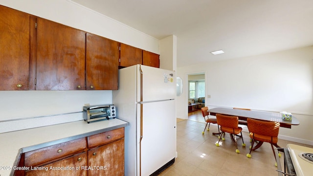5120 Wardcliff Dr, East Lansing, MI 48823 - kitchen featuring freestanding refrigerator, light countertops, stove, brown cabinetry, and baseboards