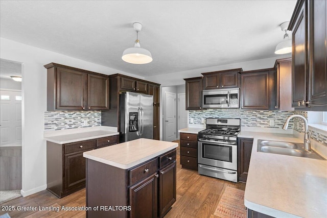 kitchen with appliances with stainless steel finishes, a sink, light countertops, and dark brown cabinetry