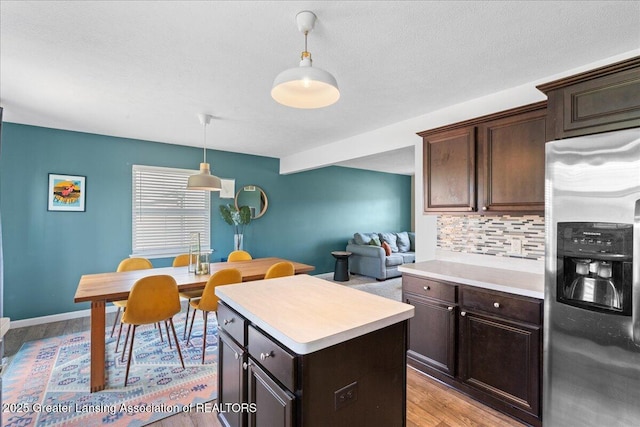 kitchen with stainless steel fridge, light wood-type flooring, light countertops, decorative backsplash, and hanging light fixtures