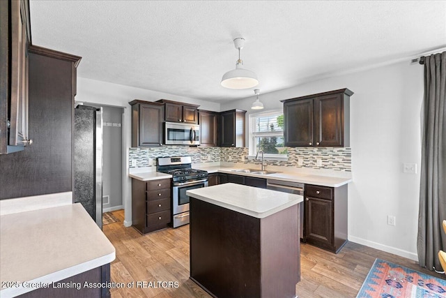 kitchen featuring appliances with stainless steel finishes, a sink, backsplash, light countertops, and dark brown cabinets
