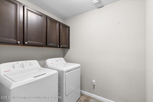 laundry area with cabinet space, washing machine and clothes dryer, baseboards, and light wood-type flooring