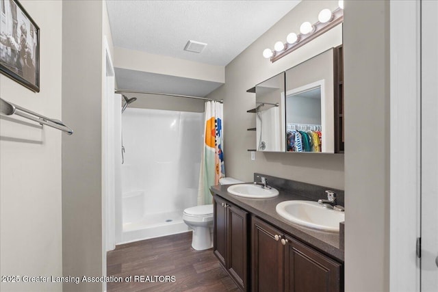 full bathroom with a shower stall, wood finished floors, toilet, double vanity, and a spacious closet