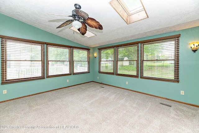 carpeted spare room with lofted ceiling, a textured ceiling, ceiling fan, a skylight, and baseboards