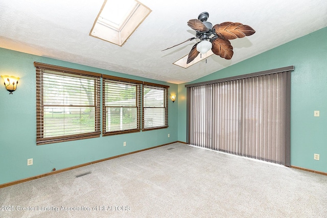 carpeted spare room featuring a skylight, lofted ceiling, ceiling fan, baseboards, and a textured ceiling