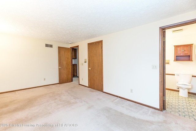 unfurnished bedroom with light carpet, a textured ceiling, ensuite bathroom, and baseboards