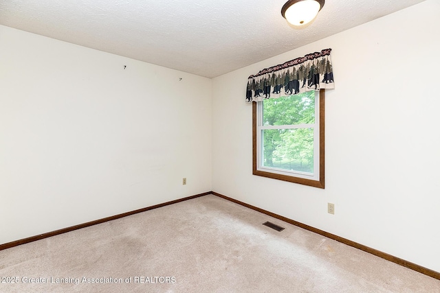 spare room featuring light carpet, baseboards, and a textured ceiling