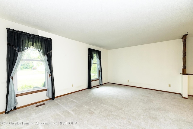 empty room featuring light carpet, baseboards, and a textured ceiling