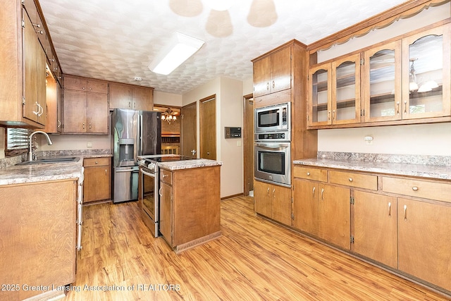 kitchen featuring appliances with stainless steel finishes, a sink, a center island, light wood-style floors, and light countertops