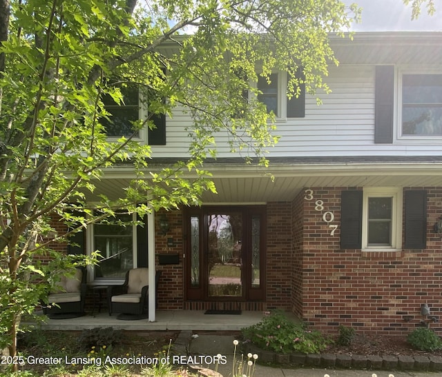 entrance to property with a porch and brick siding