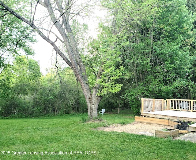view of grassy yard featuring a wooden deck and a forest view