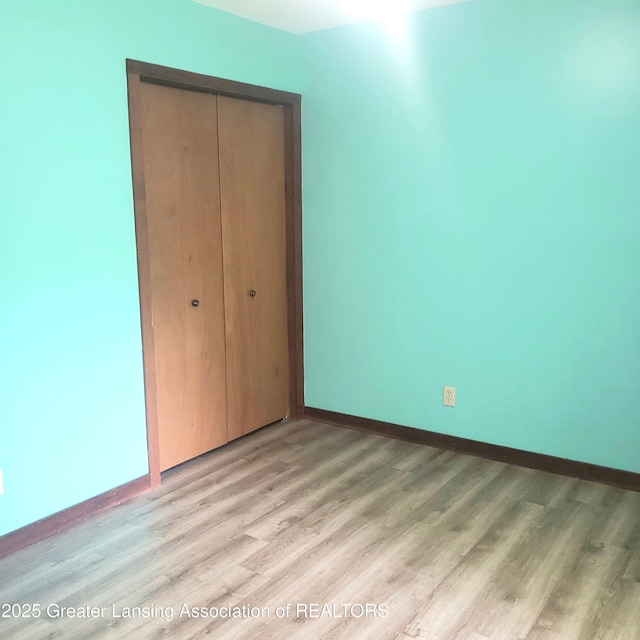 unfurnished bedroom featuring a closet, baseboards, and light wood finished floors