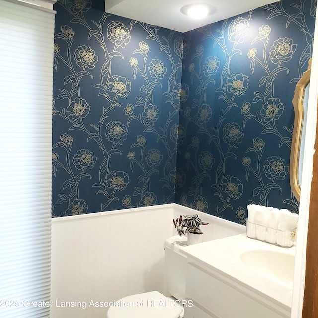half bath with wallpapered walls, toilet, and vanity