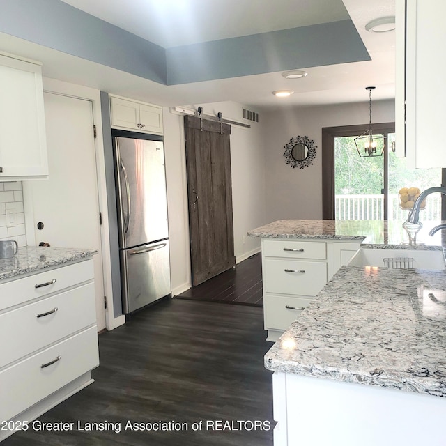 kitchen featuring freestanding refrigerator, a barn door, white cabinetry, tasteful backsplash, and a peninsula