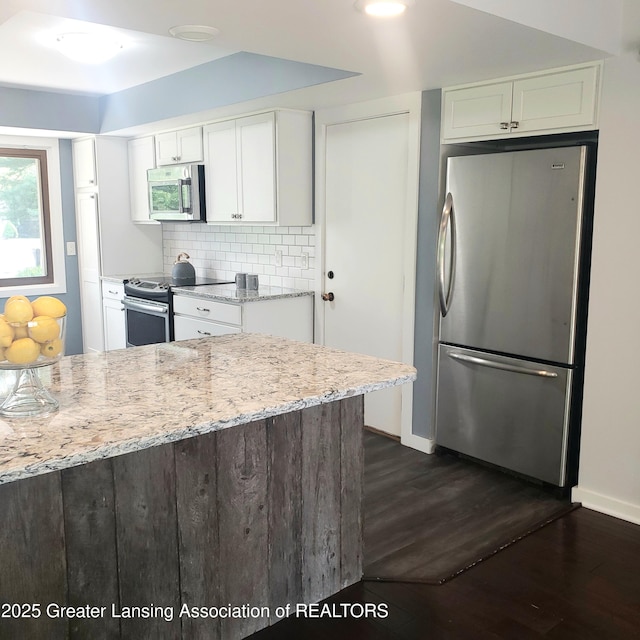 kitchen featuring appliances with stainless steel finishes, white cabinetry, dark wood finished floors, light stone countertops, and decorative backsplash