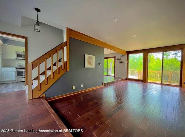 unfurnished living room featuring dark wood-style flooring, plenty of natural light, stairway, and baseboards