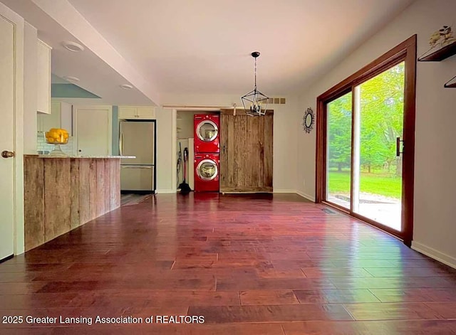 unfurnished dining area with stacked washer / dryer, dark wood-type flooring, baseboards, and a chandelier