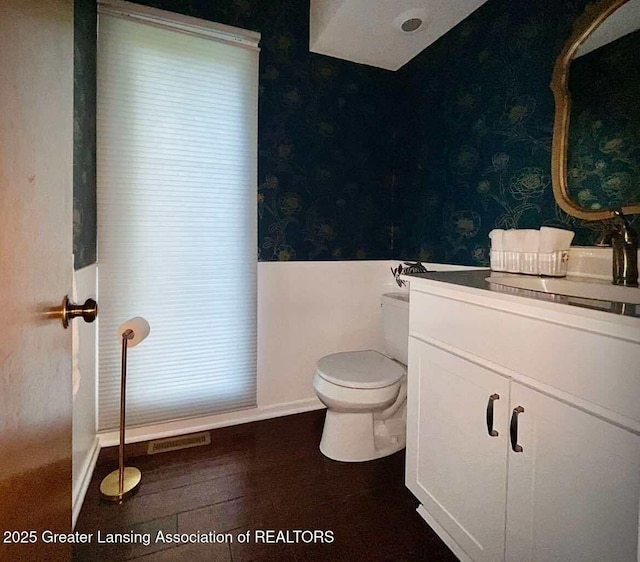bathroom featuring wallpapered walls, baseboards, vanity, toilet, and a wainscoted wall