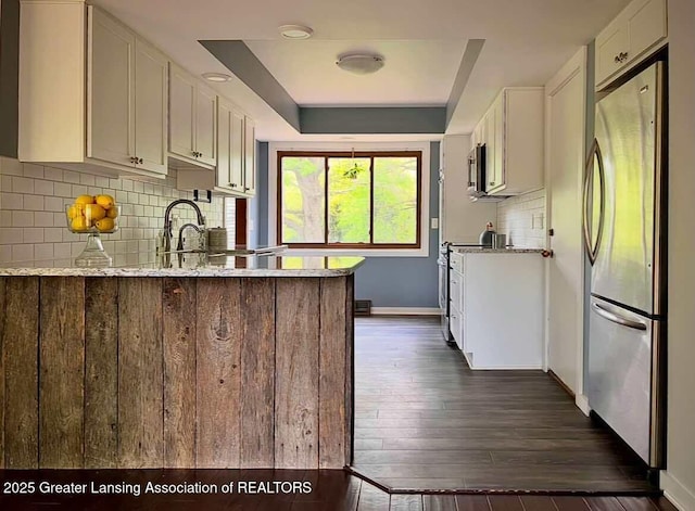 kitchen featuring appliances with stainless steel finishes, baseboards, a raised ceiling, white cabinetry, and decorative backsplash