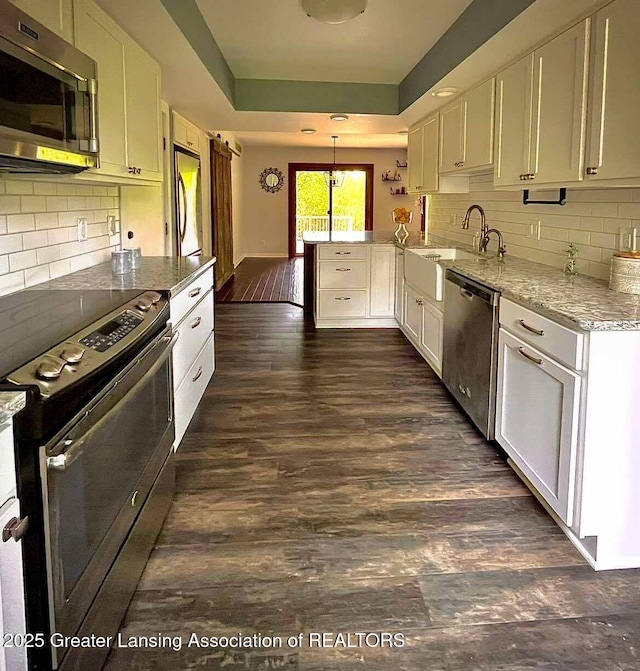 kitchen with appliances with stainless steel finishes, a sink, a raised ceiling, a peninsula, and white cabinets
