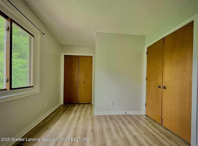 unfurnished bedroom featuring light wood finished floors, multiple windows, baseboards, and a closet