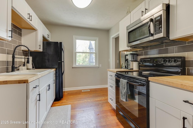 316 Union St, Grand Ledge, MI 48837 - kitchen featuring black electric range oven, butcher block counters, stainless steel microwave, a sink, and backsplash
