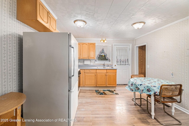 kitchen featuring freestanding refrigerator, wallpapered walls, light wood-type flooring, a sink, and light countertops