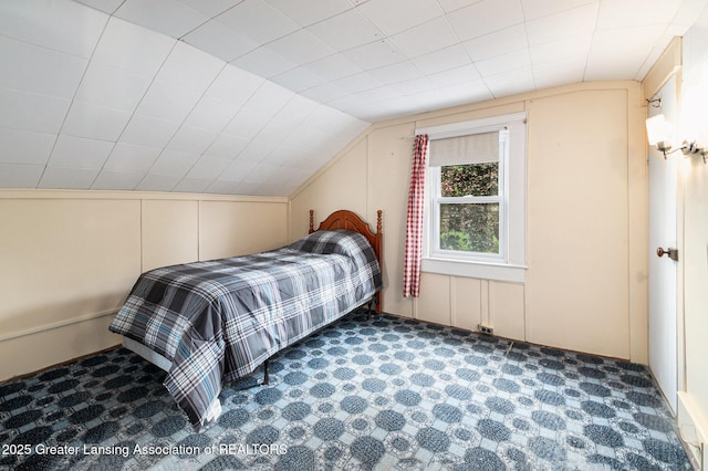 bedroom with lofted ceiling, a decorative wall, and carpet floors