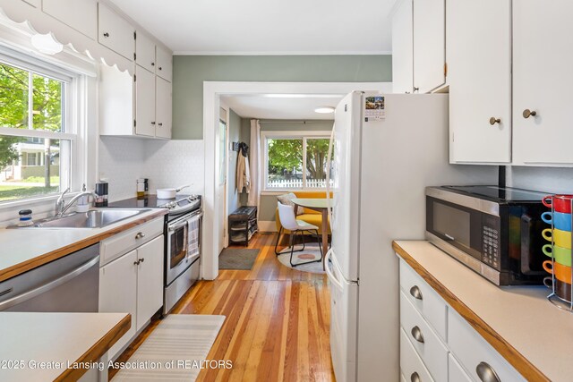 1038 Morgan St, Lansing, MI 48912 - kitchen with stainless steel appliances, a sink, white cabinets, light wood-type flooring, and healthy amount of natural light
