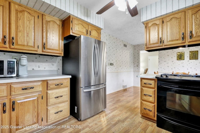 10079 Woodland Acres Dr, Grand Ledge, MI 48837 - kitchen featuring stainless steel appliances, wallpapered walls, wainscoting, light wood-type flooring, and ceiling fan