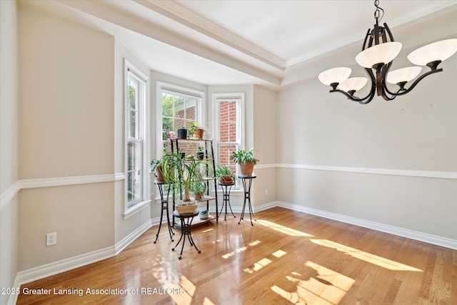 living area featuring a chandelier, light wood-style floors, baseboards, ornamental molding, and a raised ceiling