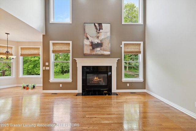unfurnished living room with wood finished floors, a high ceiling, a tile fireplace, plenty of natural light, and baseboards