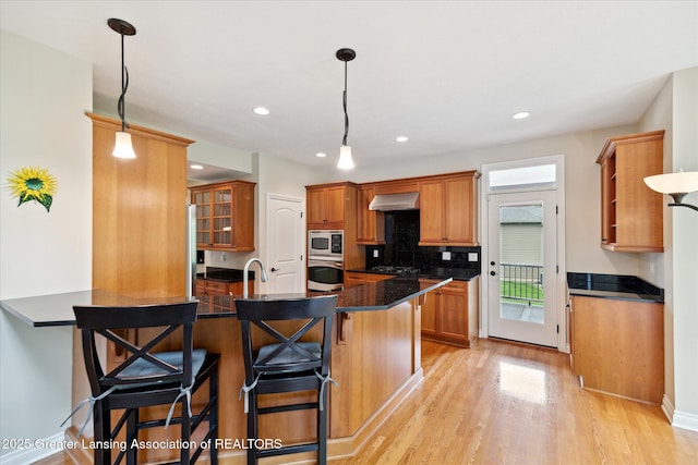 kitchen featuring stainless steel appliances, extractor fan, a kitchen breakfast bar, brown cabinetry, and recessed lighting