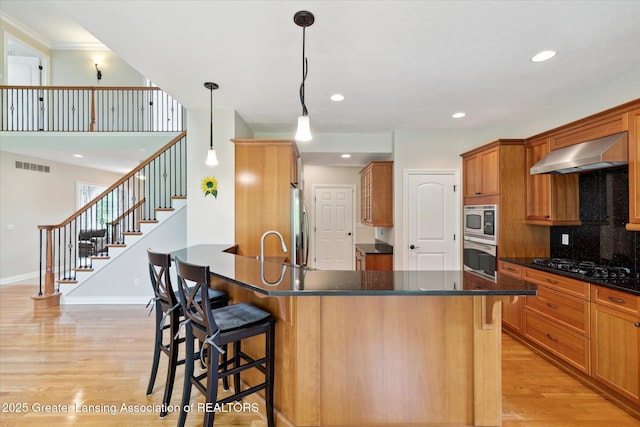 kitchen featuring wall chimney exhaust hood, appliances with stainless steel finishes, light wood-type flooring, a breakfast bar area, and recessed lighting