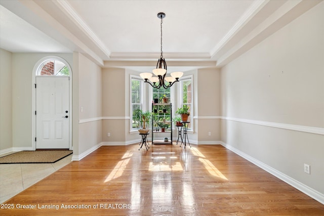 entrance foyer featuring a chandelier, a tray ceiling, crown molding, wood finished floors, and baseboards
