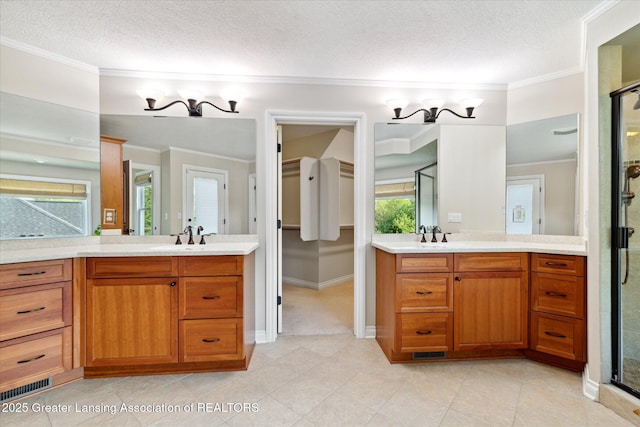 full bathroom featuring a textured ceiling, a shower stall, ornamental molding, two vanities, and baseboards