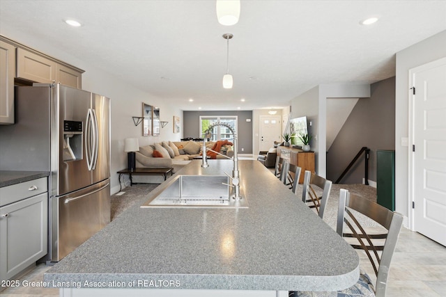 3842 Fossum Ln, Okemos, MI 48864 - kitchen featuring stainless steel fridge, a sink, a center island with sink, open floor plan, and hanging light fixtures