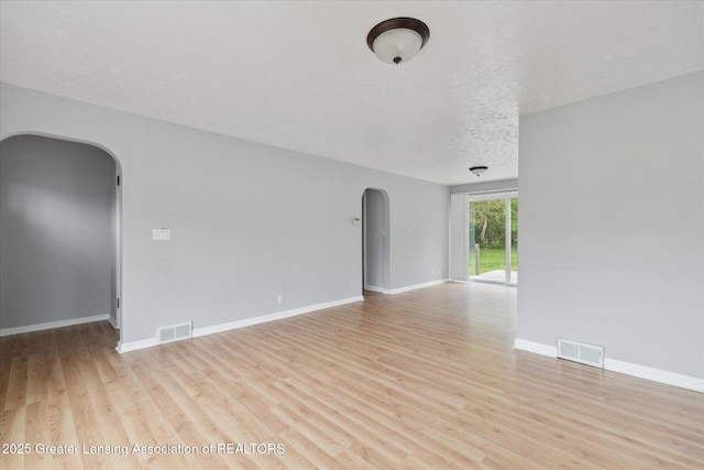 2468 Lansing Rd, Charlotte, MI 48813 - empty room featuring arched walkways, light wood-type flooring, baseboards, and a textured ceiling