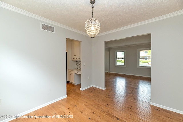 3979 Dayspring Ct, Okemos, MI 48864 - unfurnished room with a chandelier, light wood-style flooring, ornamental molding, a textured ceiling, and baseboards