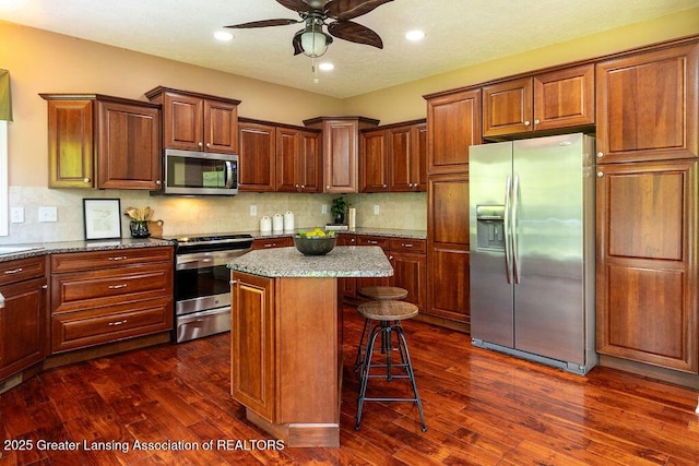 4655 Dimond Way, Dimondale, MI 48821 - kitchen featuring appliances with stainless steel finishes, a ceiling fan, a kitchen island, a breakfast bar, and dark wood-style floors